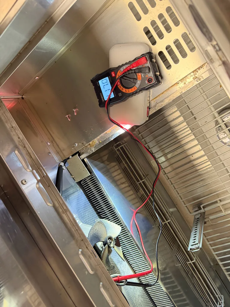 Multimeter testing an evaporator fan in a Turbo Air prep table
